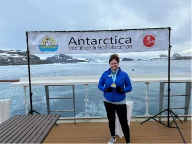 Leigh Ann Schultz on a boat standing under the Marathon banner with the Antarctica scenery behind